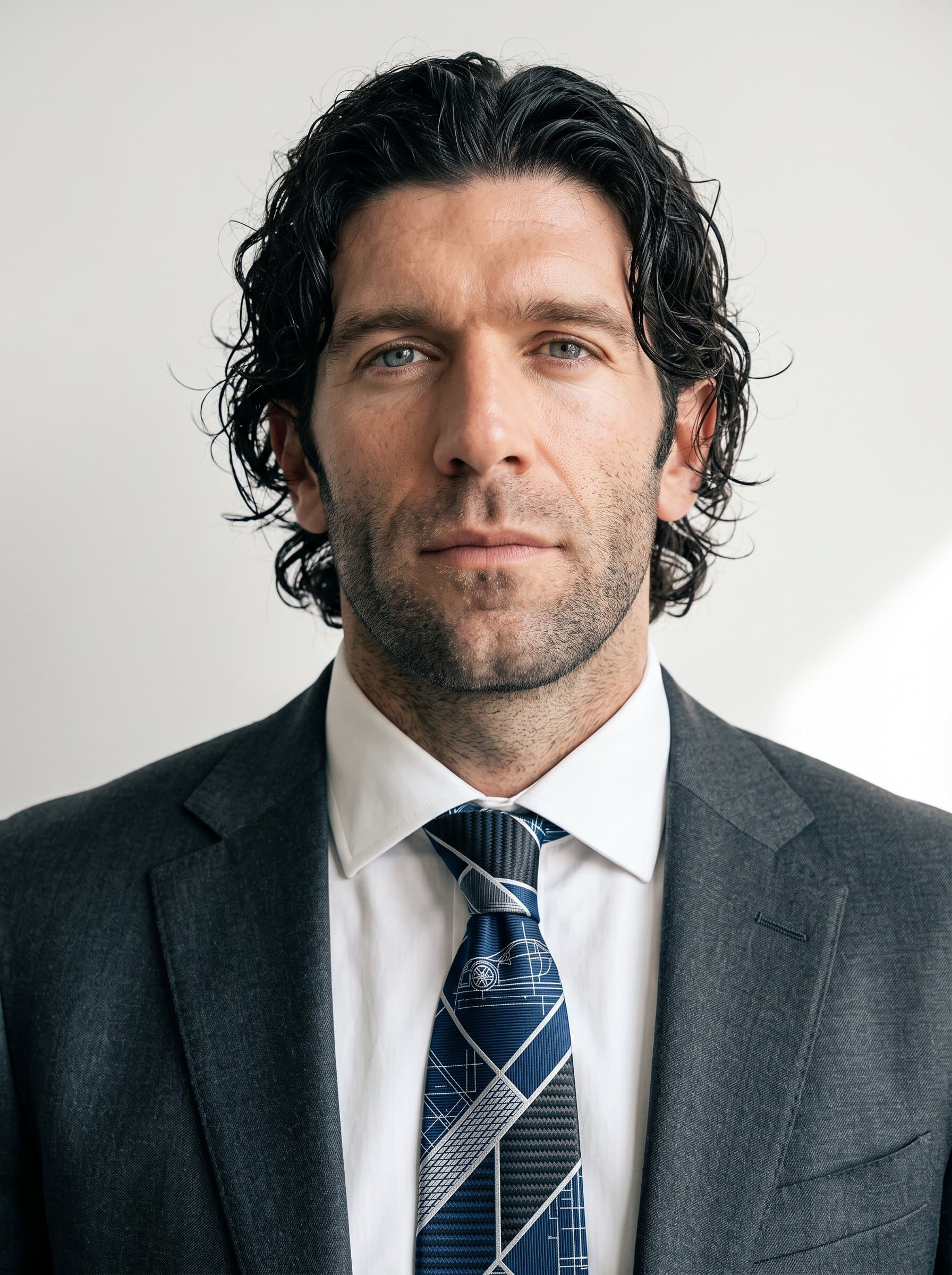 : Headshot of an man sporting a geometric-patterned tie, reminiscent of car designs. The minimalist background brings focus to their determined expression, conveying leadership in automotive design.