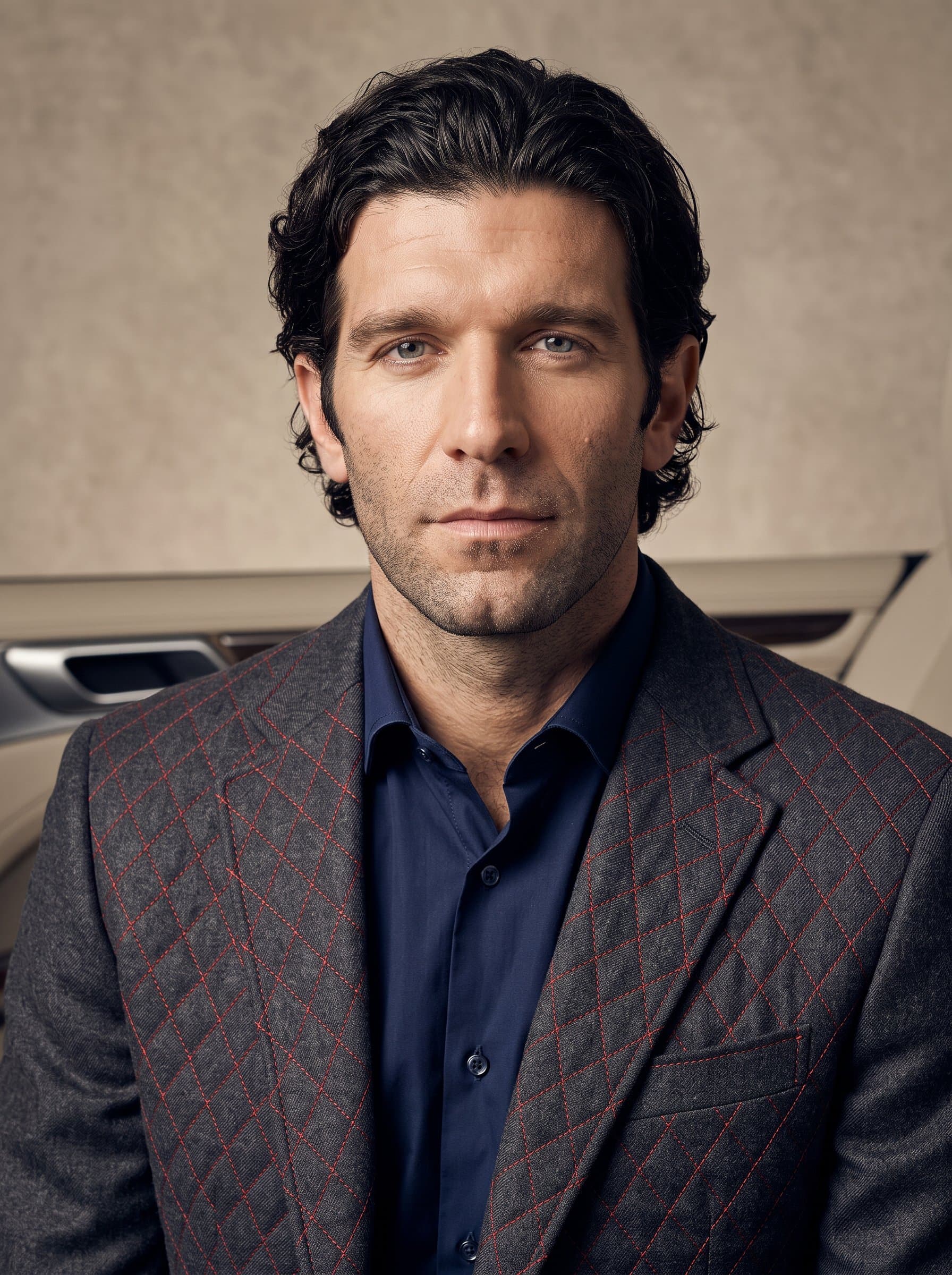 : A headshot of an man wearing a textured blazer with a fine patterned stitch resembling car upholstery, standing against an understated backdrop, exuding professionalism in automotive interiors.