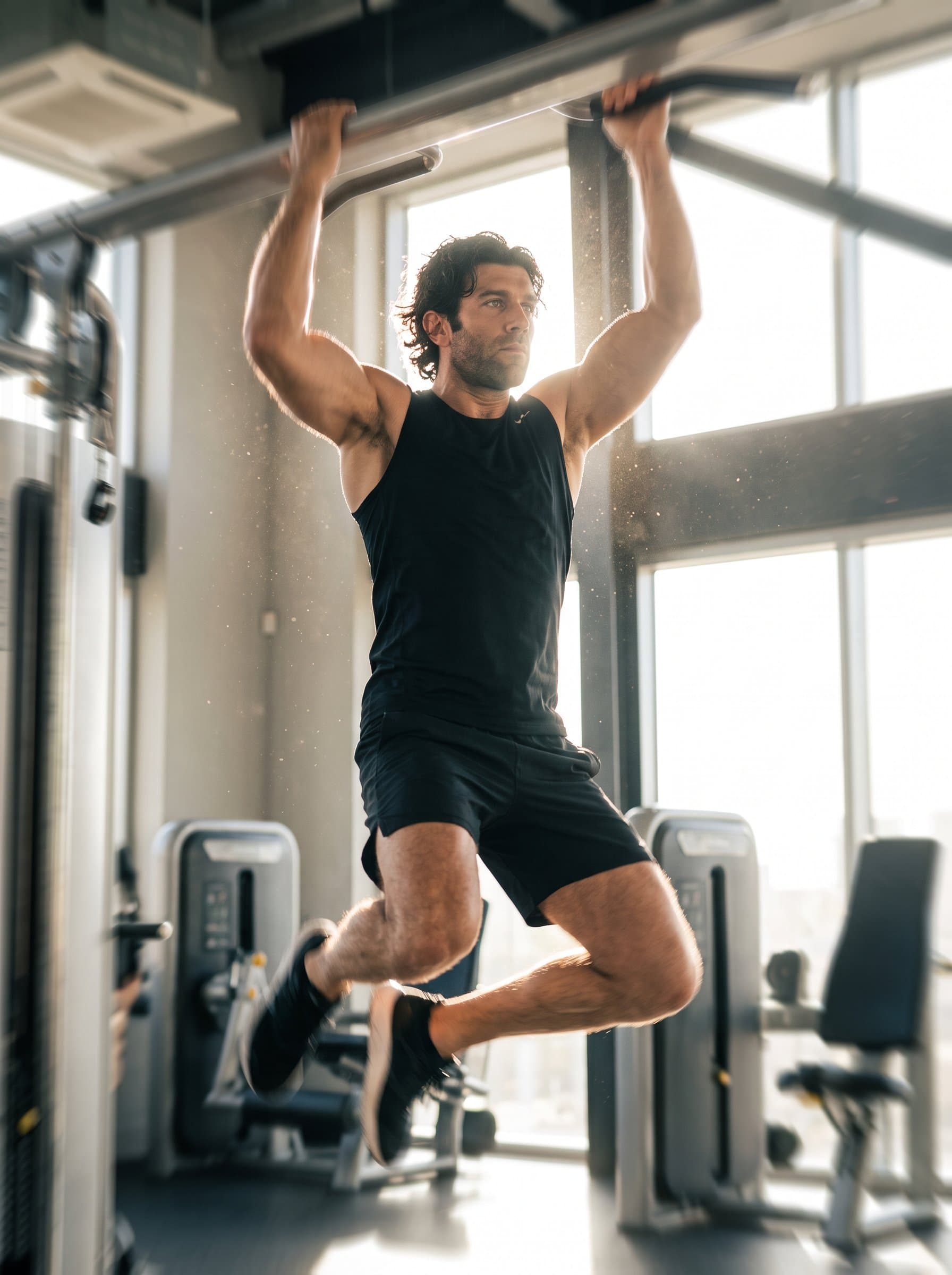 performing a high-intensity workout move in mid-air, captured with motion blur to highlight energy and agility, set in a modern gym with bright, natural light streaming through windows.