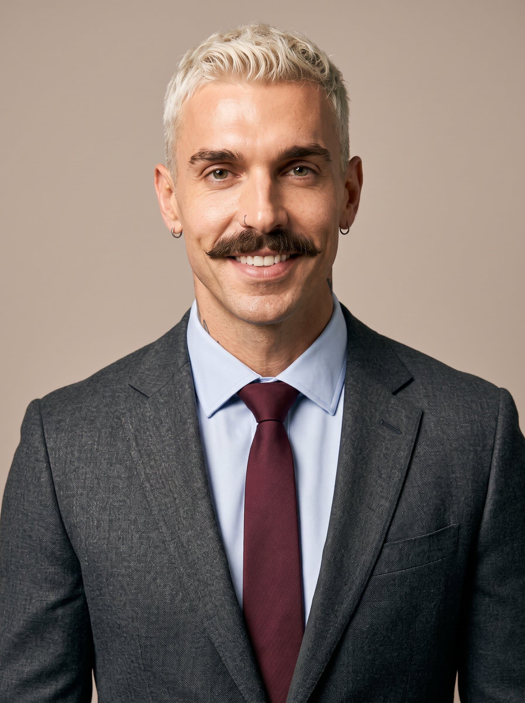 : Assemble a university faculty headshot where the man is dressed in a professional attire of choice, placed against a light taupe backdrop. Warm lighting enhances their self-assured and pleasant demeanor.
