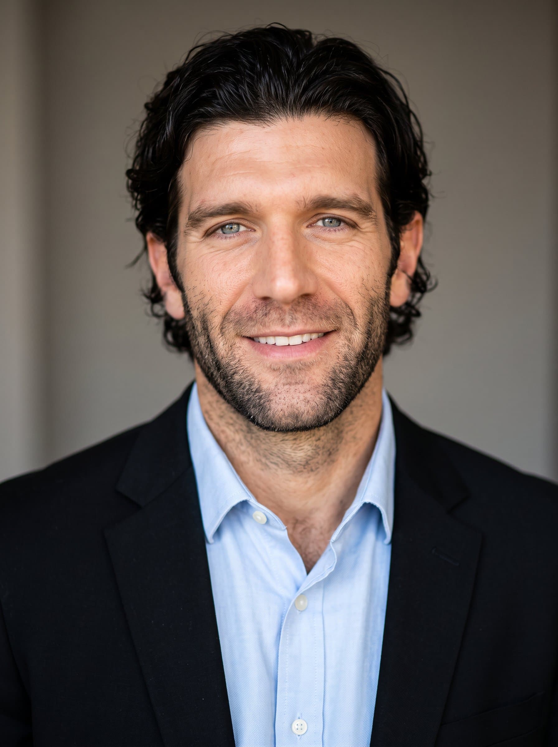 : Illustrate a headshot with a faculty member in a classic black blazer and light shirt, against a neutral backdrop. The warm lighting accentuates a confident and approachable demeanor ideal for university settings.
