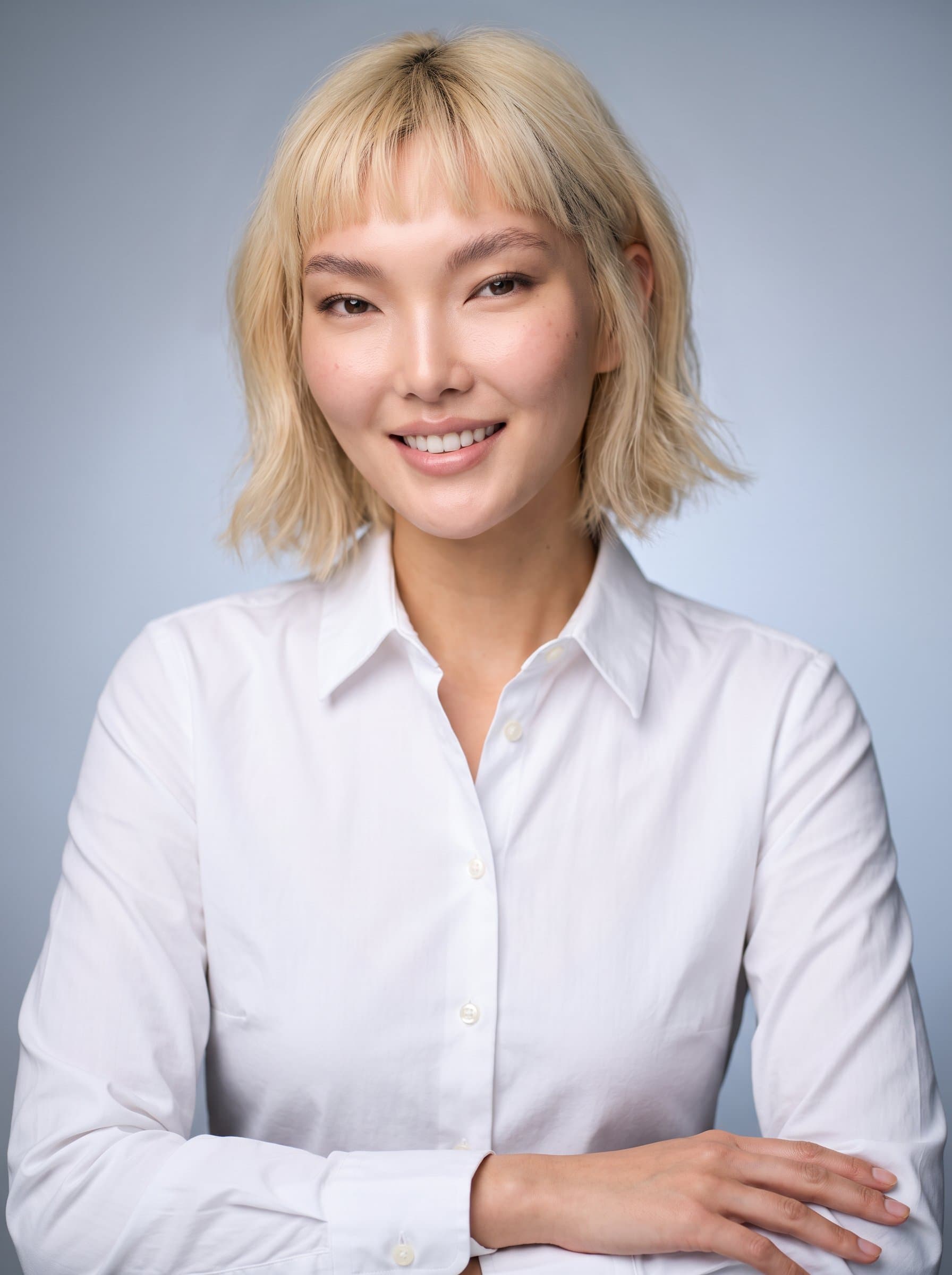: Wearing a formal dress shirt, an woman poses against a gradient backdrop. Their poised posture and warm smile with subtle lighting reflect an approachable yet professional character.