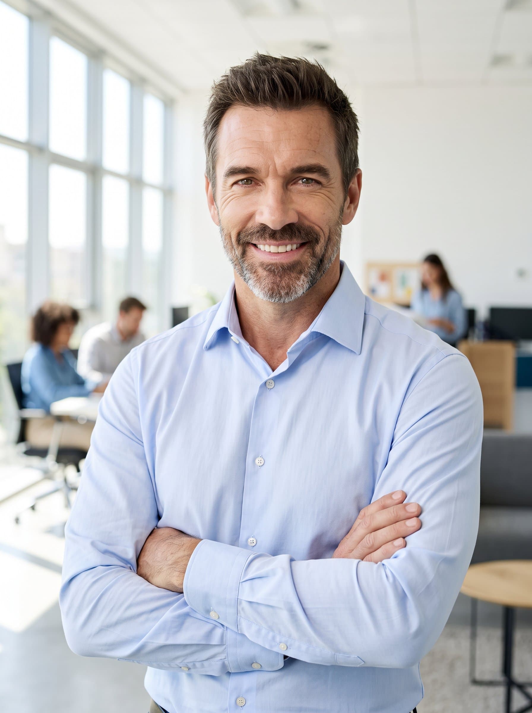 : A professional man in a collared shirt poses in front of a light-filled office space. Their confident stance and engaging smile ensure a welcoming, competent LinkedIn presentation.