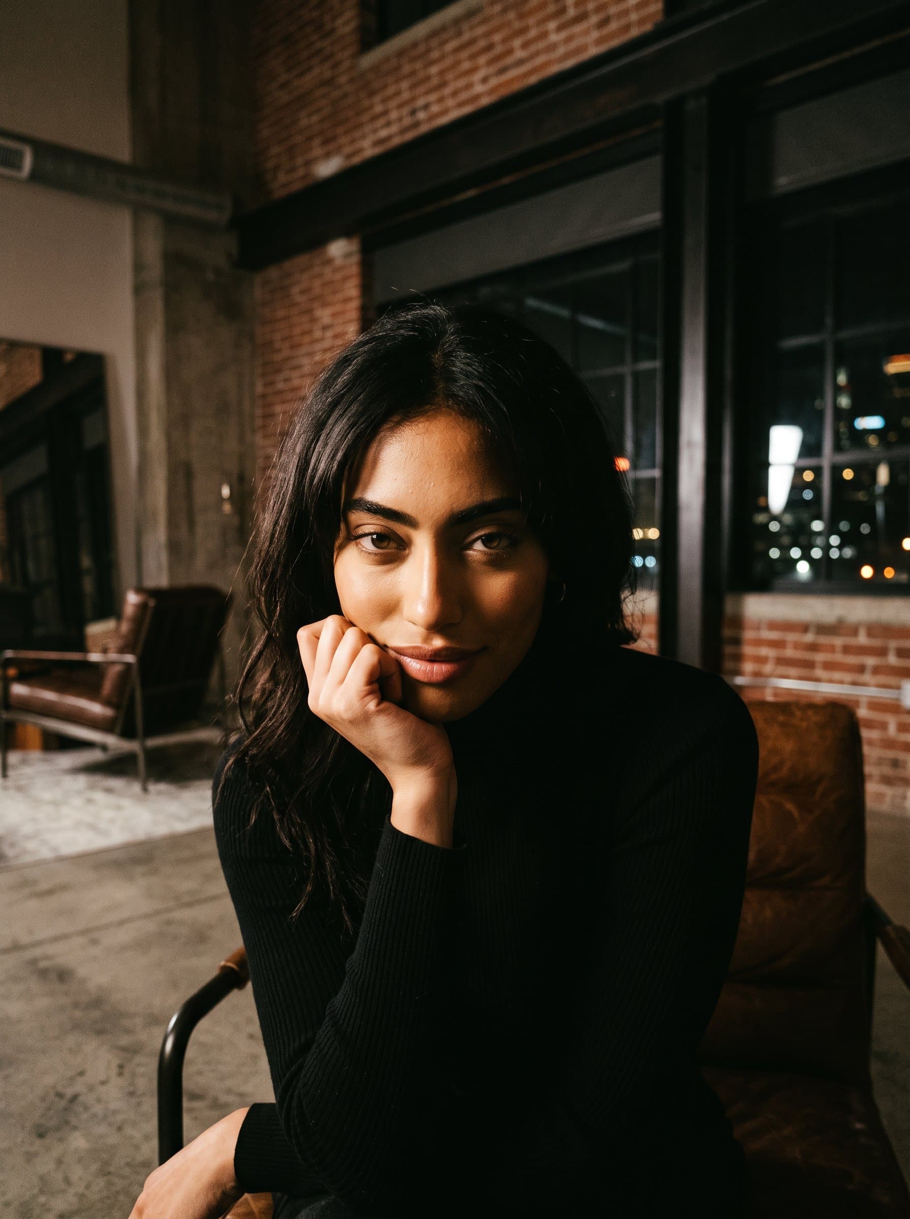 : Design a captivating, moody portrait with dramatic lighting in a modern loft, perfect for a mysterious and intriguing Tinder profile picture.