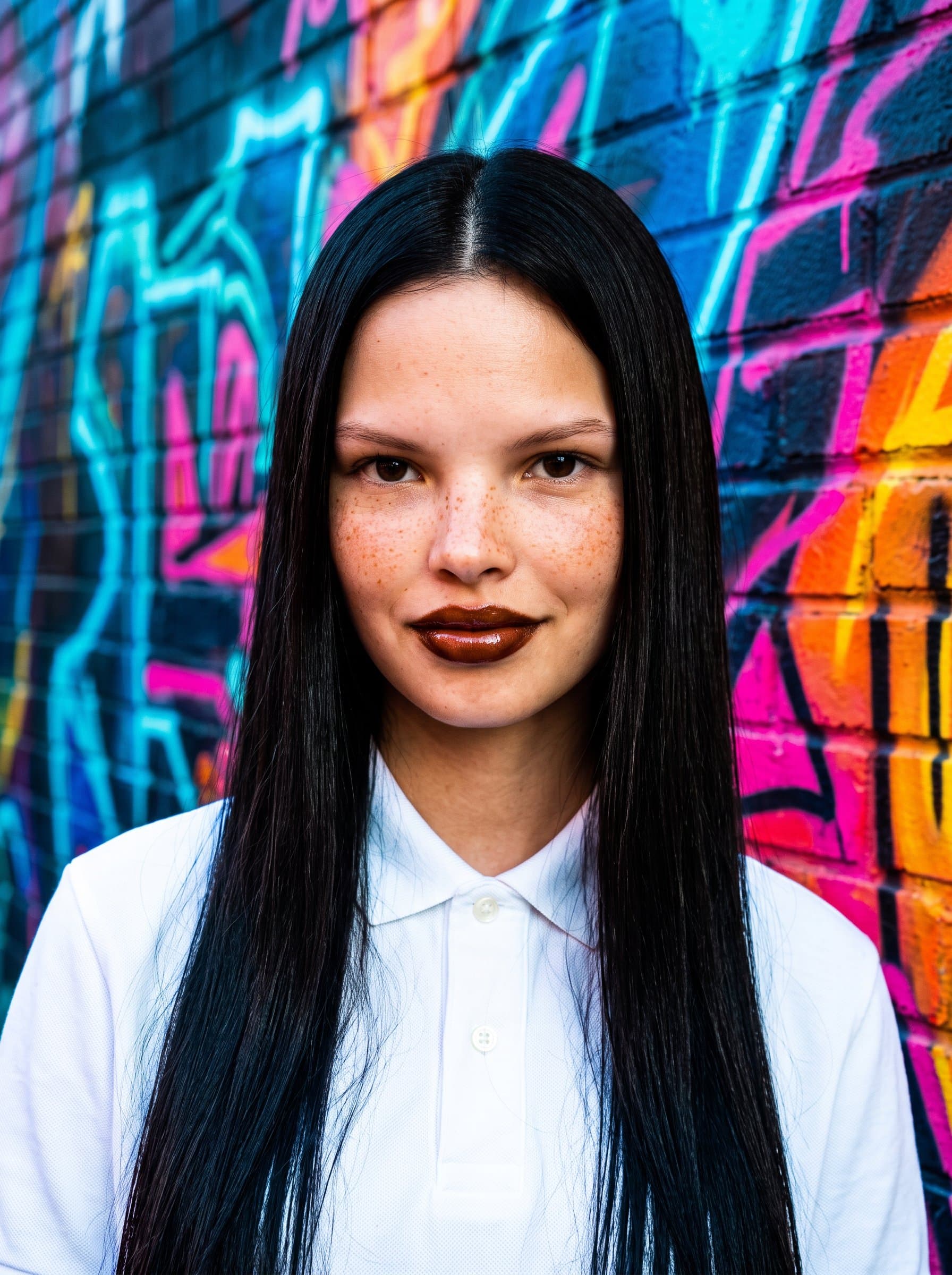 : Create a headshot with vibrant graffiti art in the background, emphasizing the woman's bold and creative personality. Use dynamic lighting to enhance the energetic and urban vibe.