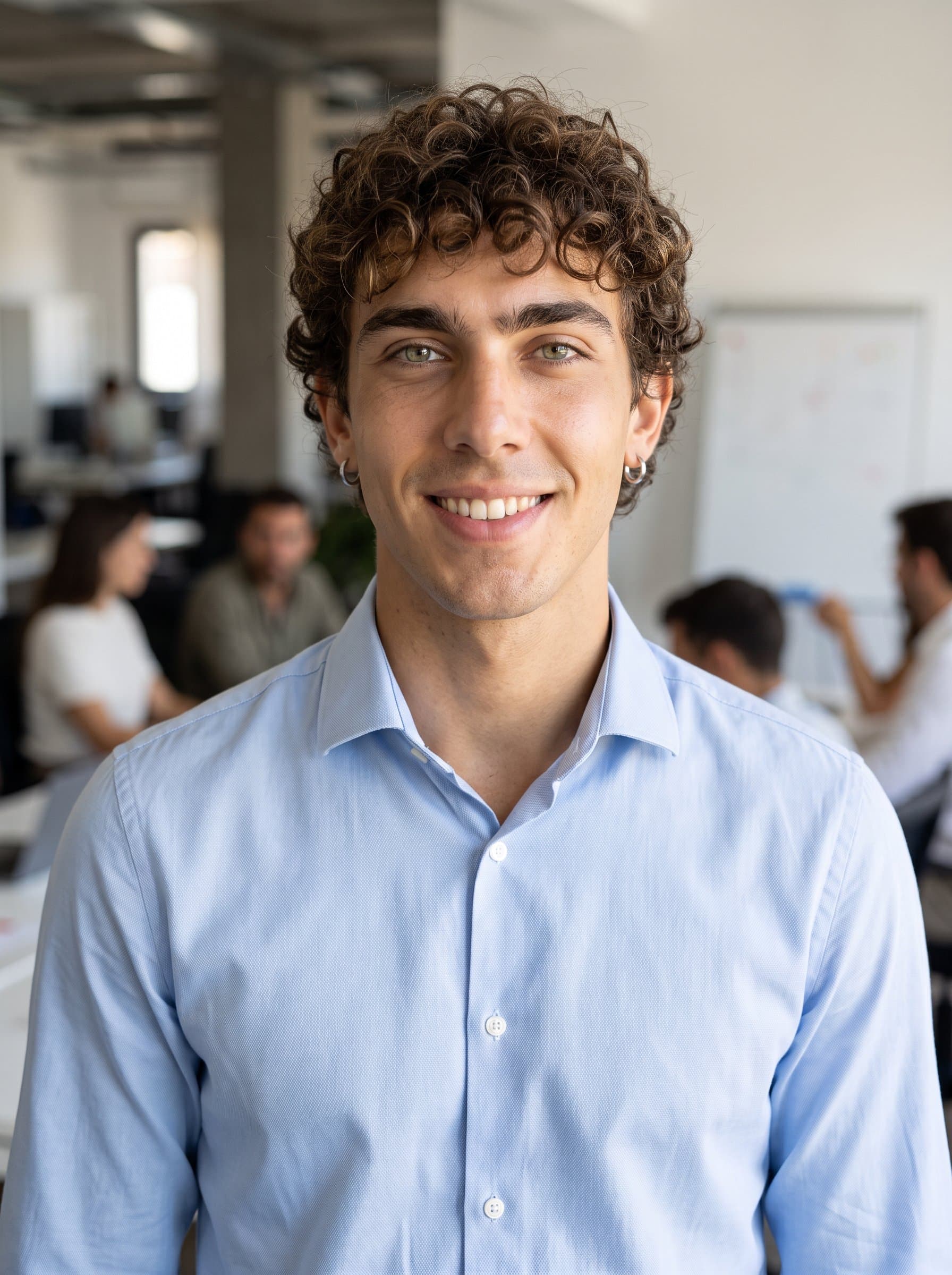 : Generate a polished headshot with an open office background. The man sports a light blue collared shirt, projecting a friendly yet professional demeanor ideal for corporate resumes.