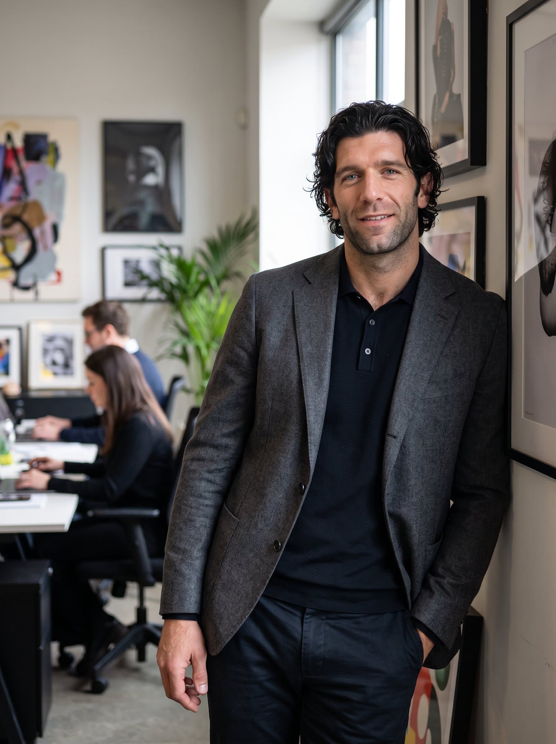 Render a image of a man with a relaxed posture, wearing contemporary business attire. The background should hint at a creative workspace, with art pieces softly blurred in the mix.