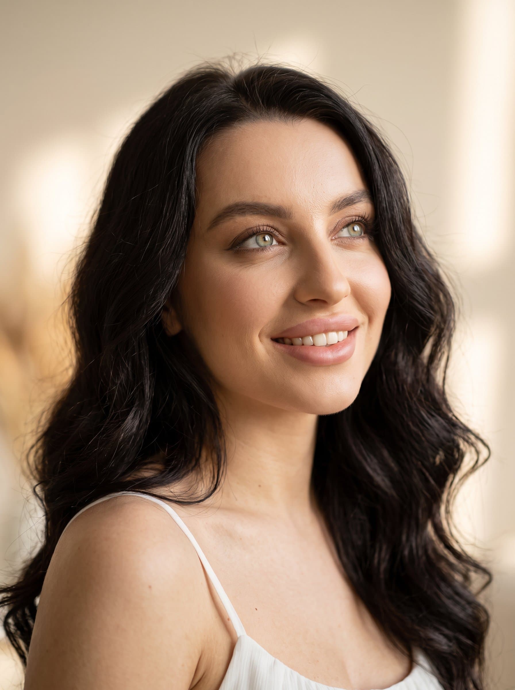 Design a headshot with an artistic angle, the woman slightly looking upwards, indicating ambition. The backdrop remains minimalistic, focusing attention on the warm, engaging facial expression.