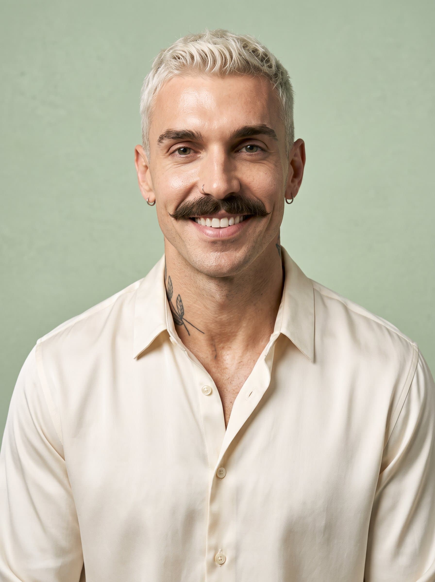 Produce a headshot where the man displays a gentle smile, wearing a simple yet elegant shirt. Position them against a neutral, pastel-colored background to create a calm and friendly impression.