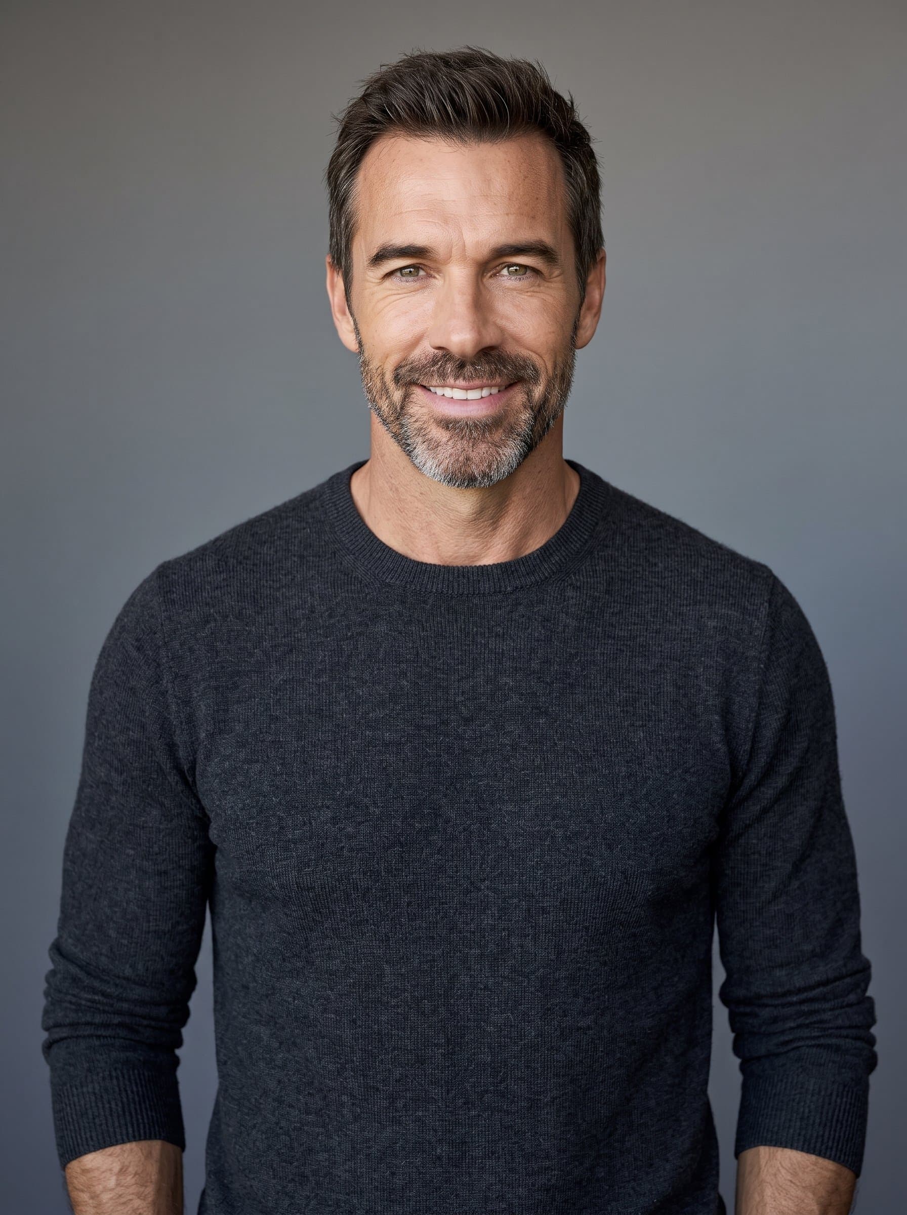 Create a headshot that exudes calmness, with a serene smile and relaxed shoulders. The man stands against a simple grey backdrop, with lighting emphasizing natural skin tones and subtle personality traits.