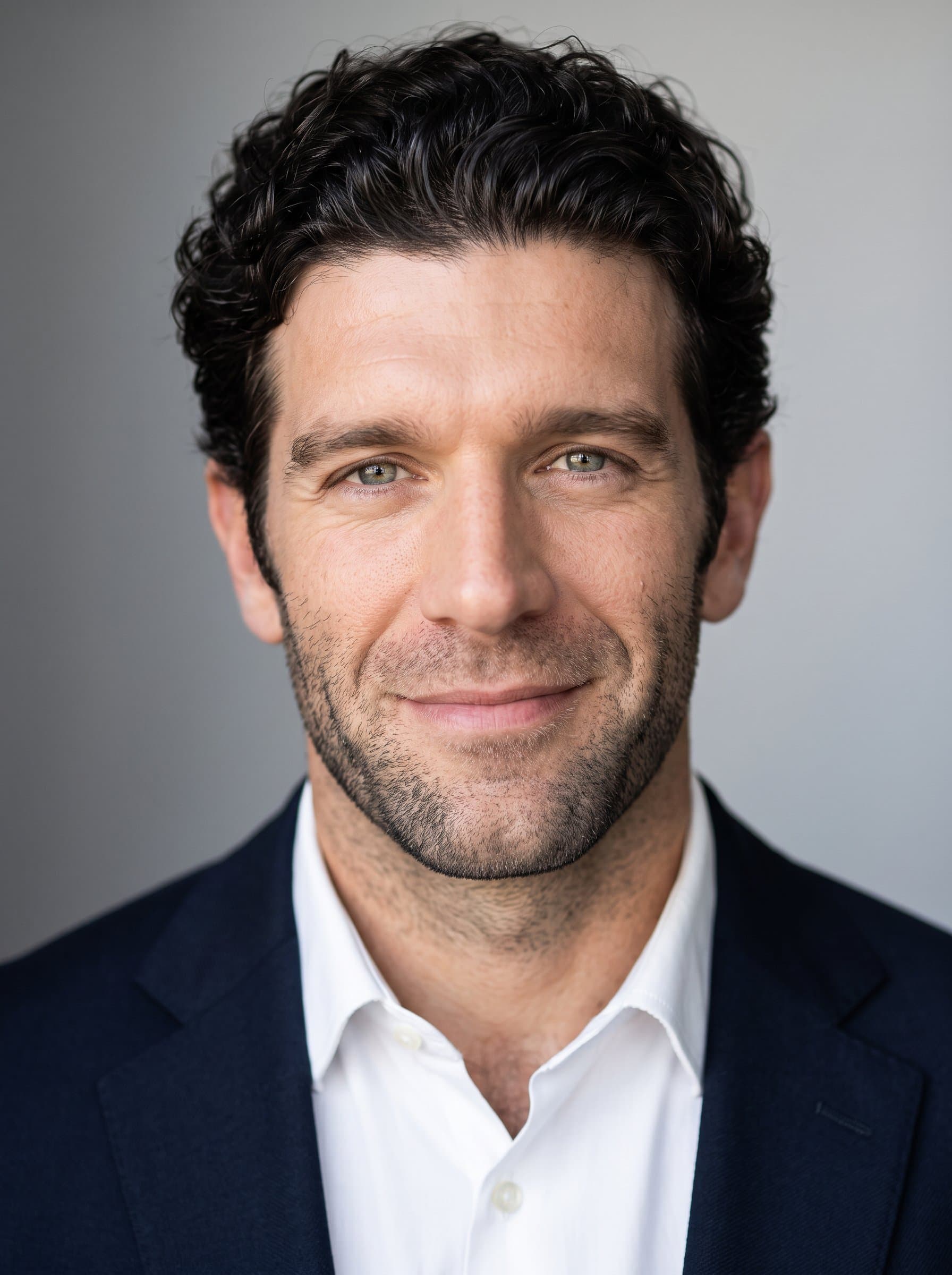 Produce a headshot where the man's face is softly illuminated, with a backdrop containing a subtle gradient. The focus remains on the friendly, professional demeanor and clear, well-defined facial features.