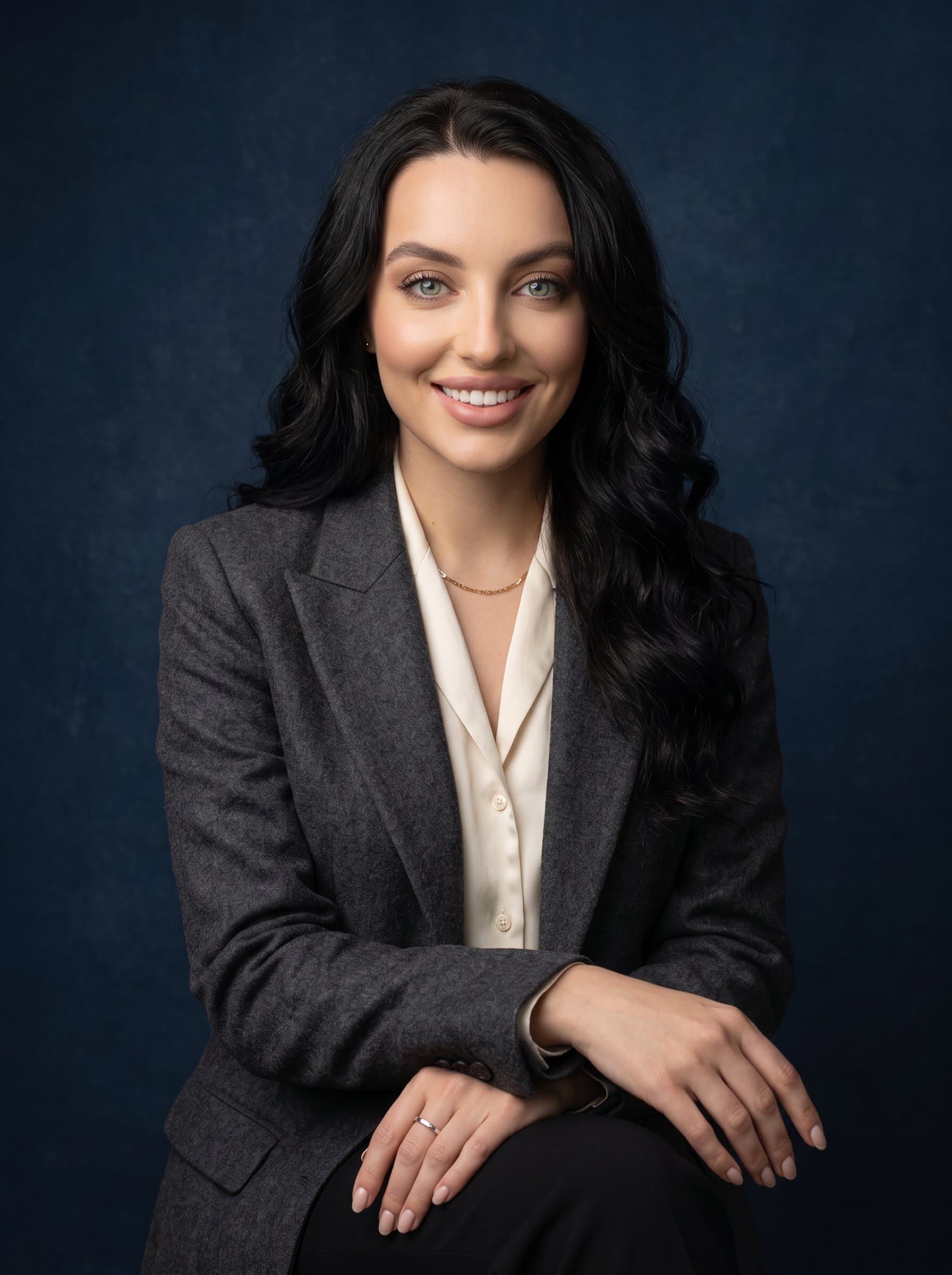 : Design a classic headshot with a timeless, elegant aesthetic. The woman sits against a textured navy background, wearing a tailored outfit, exuding poise and sophistication, ideal for professional social media use.