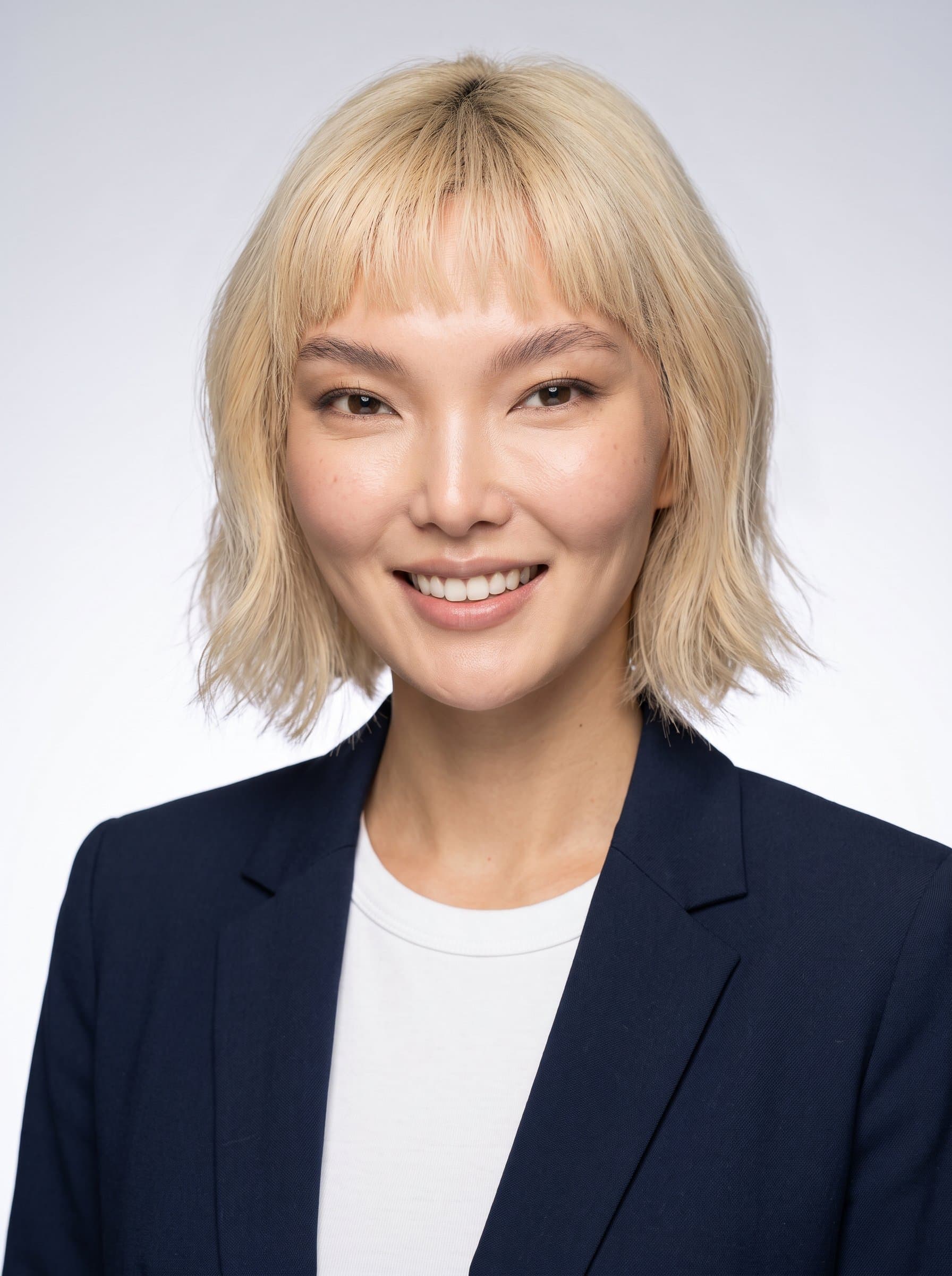 Capture a woman with a warm smile, wearing business casual attire. The background is a subtle gradient from light gray to white, emphasizing the woman's facial features and creating an air of openness.