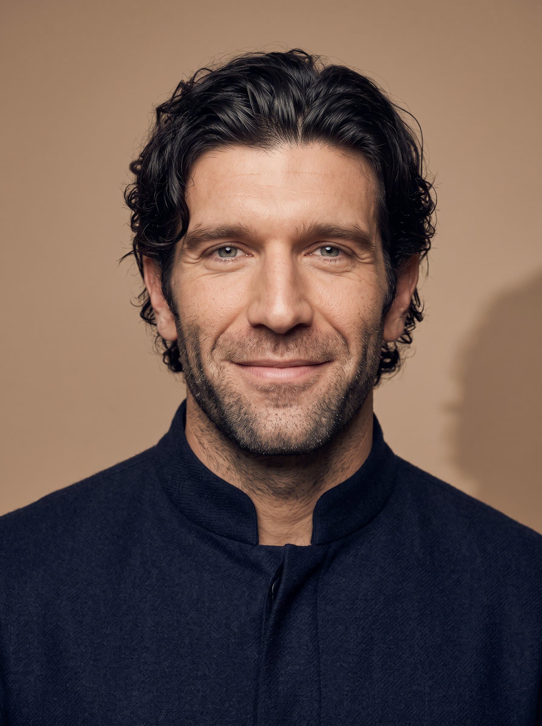 Generate a image of a man in a high-collared shirt. The neutral tan background adds sophistication, and the focus on their gentle smile engages viewers with assurance and friendliness.