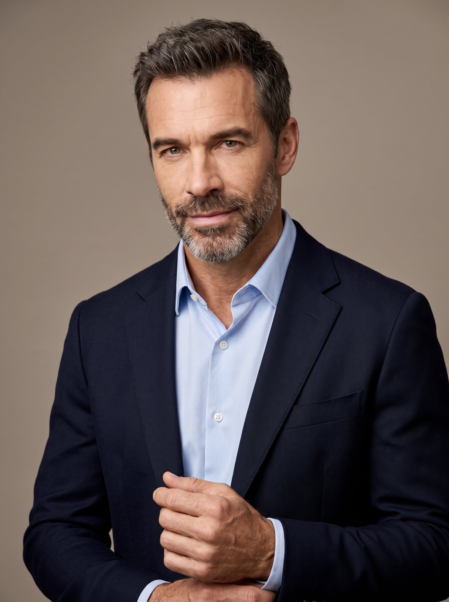 Create a portrait where the man gazes slightly to the side. The plain taupe background complements their attire, creating an engaging yet professional look for social media or business platforms.