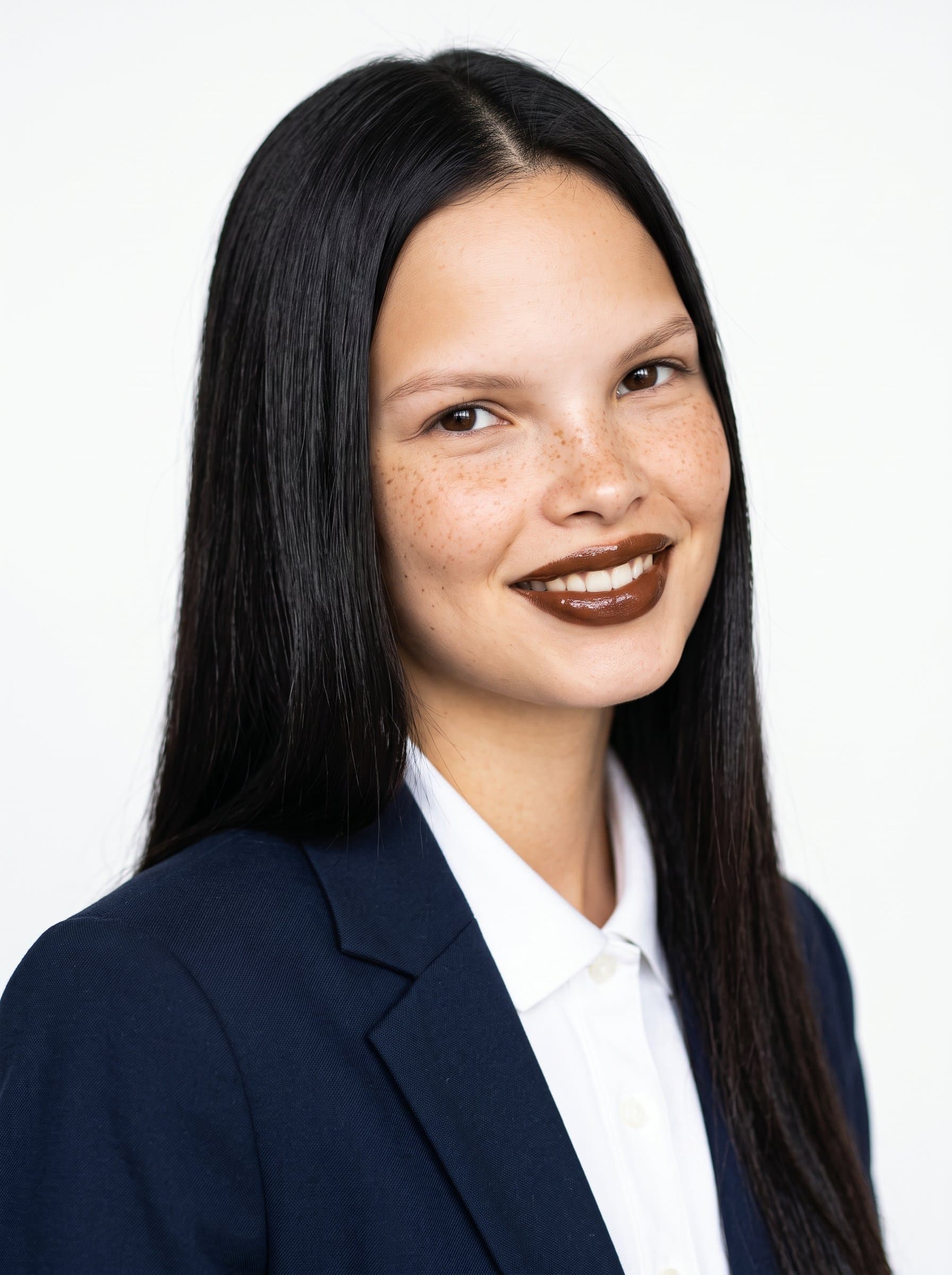 Design a headshot with a clean white backdrop. The woman wears a smart blazer, and their slight head tilt suggests approachability, while direct eye contact communicates confidence.