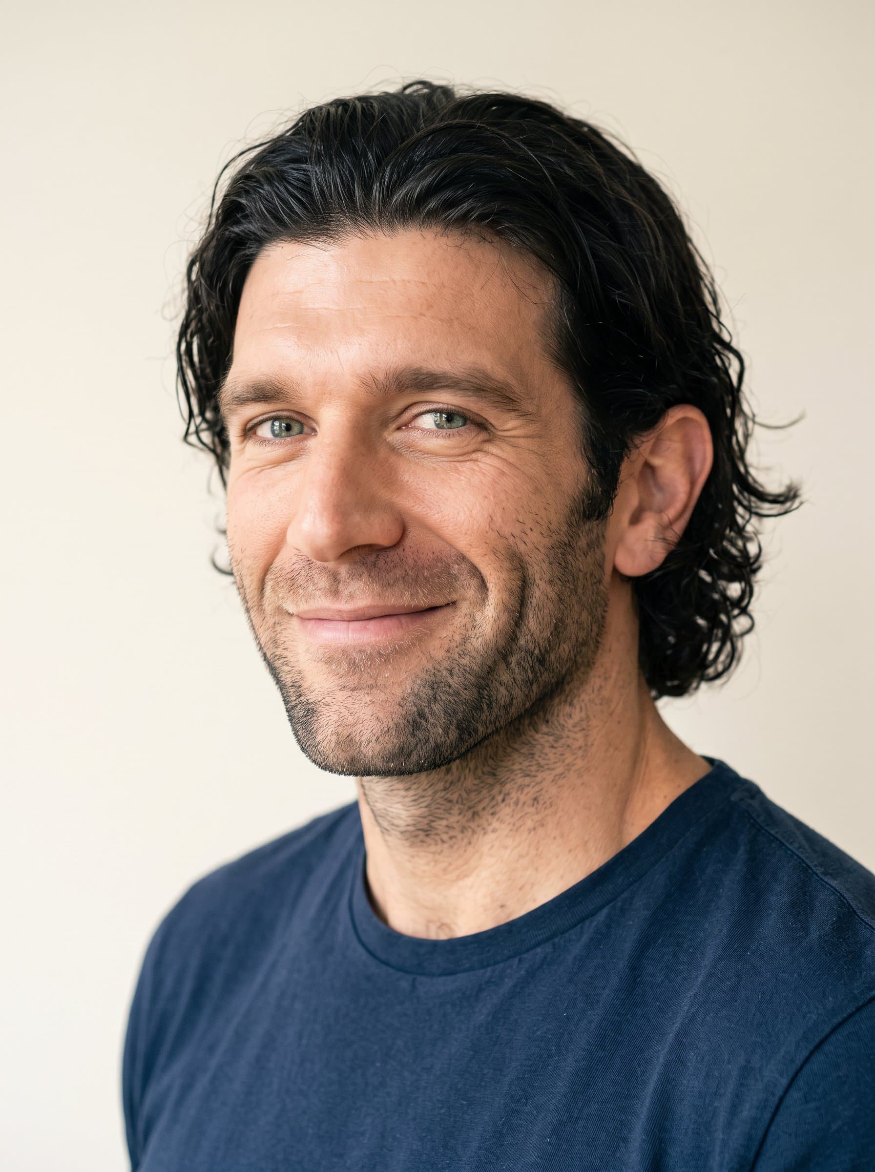 Design a profile picture of a man in a simple shirt, their head slightly turned. The neutral cream background ensures their lively eyes and friendly expression take center stage.