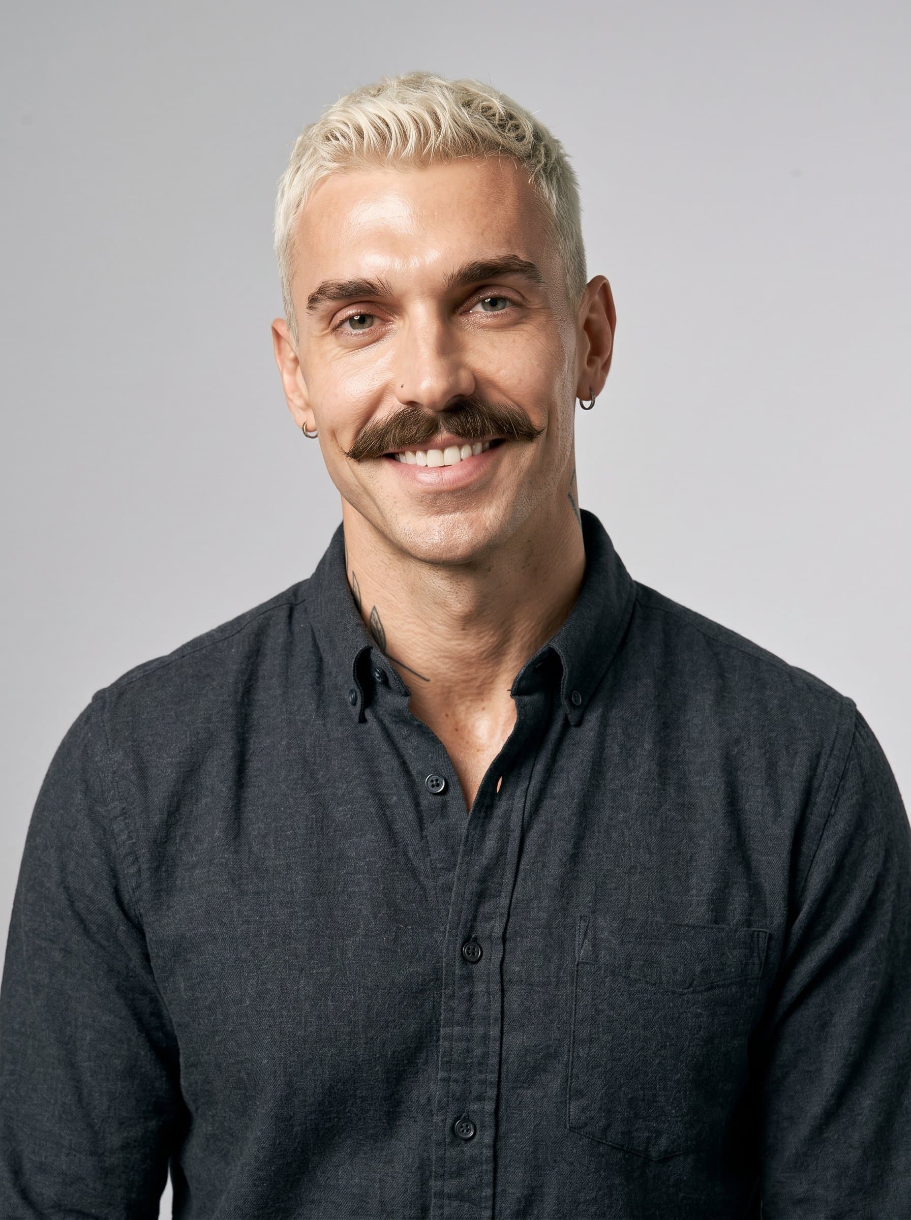 Compose a photo with a man in a dark shirt, head slightly tilted. The neutral gray backdrop enhances the warmth in their smile, making their digital persona inviting and professional.