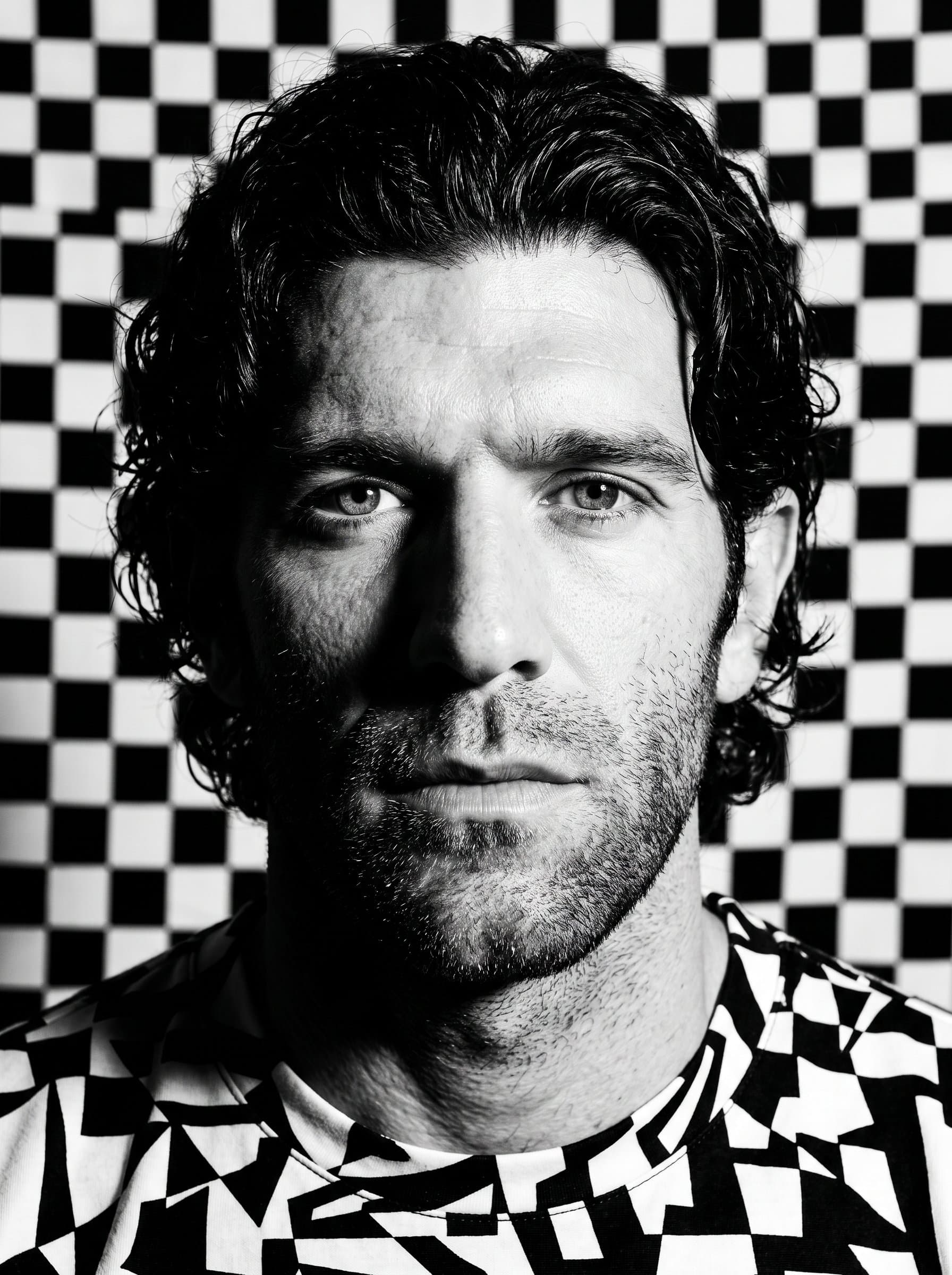 : High contrast headshot with a bold expression. Background: monochrome checkerboard. Attire: black and white patterned top. Highlight facial features with stark shadows.