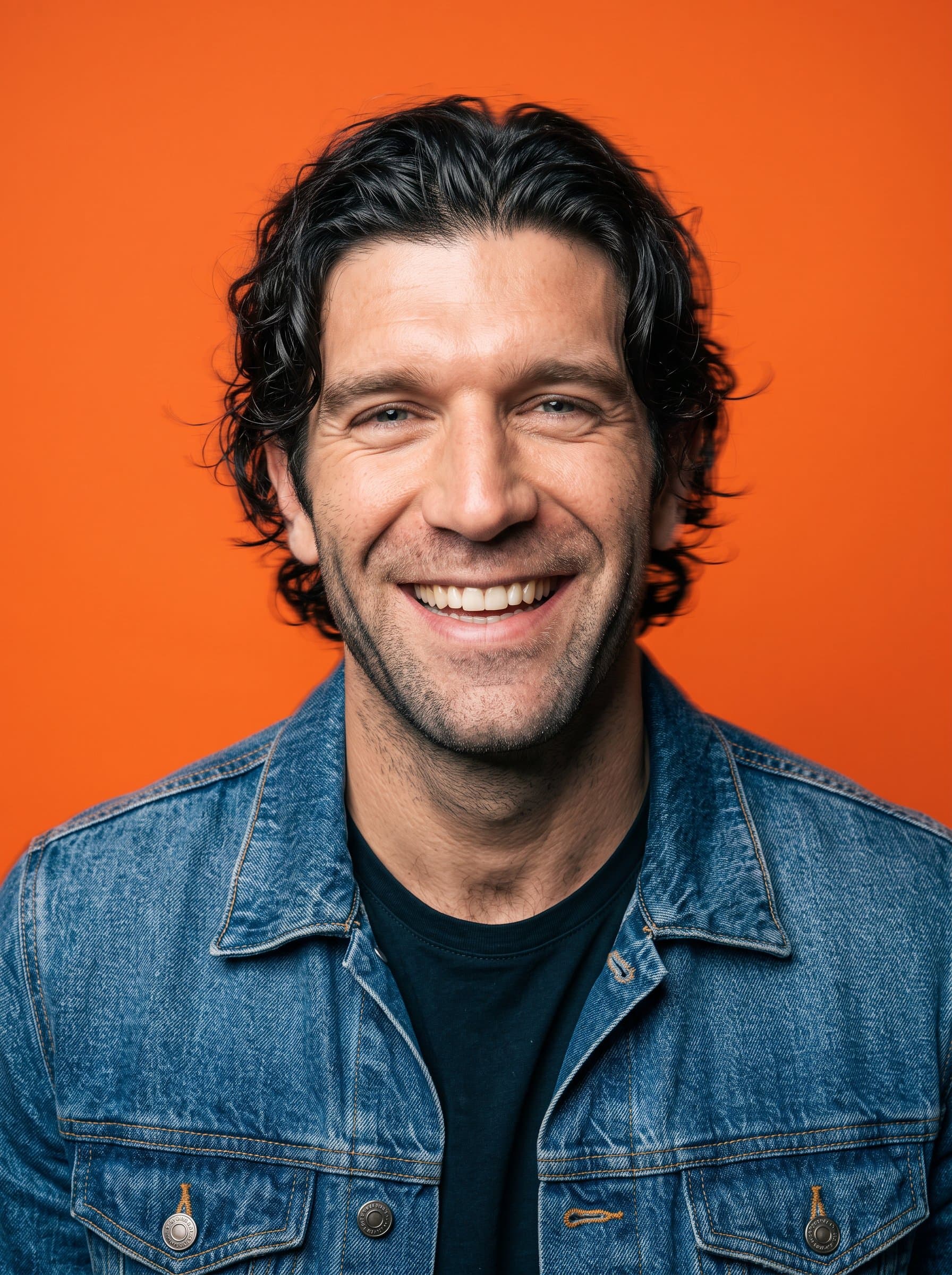 : Energetic headshot with a big, genuine smile. Background: vivid orange. Attire: casual denim jacket. Add a slight motion blur to imply dynamism and creativity.