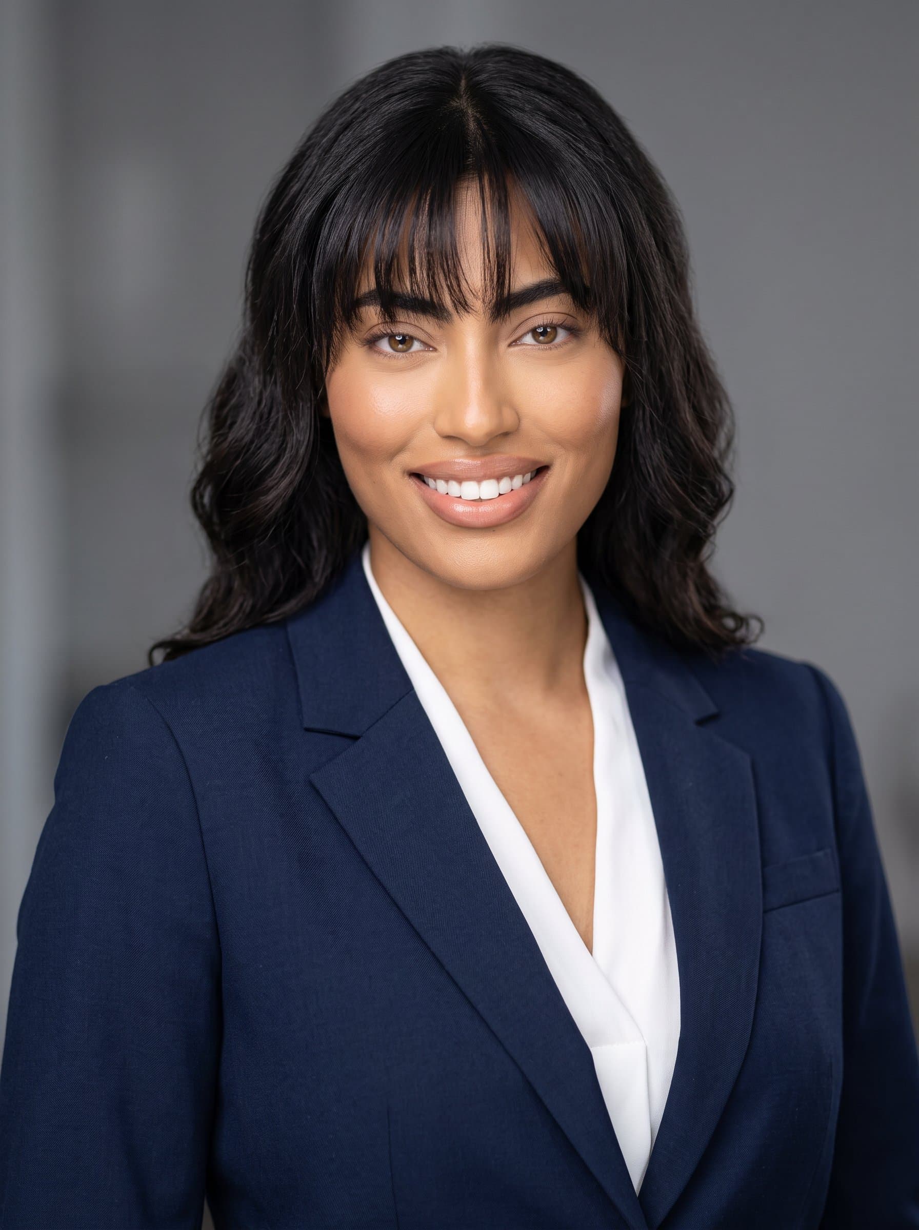 : A professional headshot for a corporate profile, capturing a confident woman in a sleek business suit, set against a neutral background. The lighting highlights their approachable demeanor, suitable for a Glassdoor profile.
