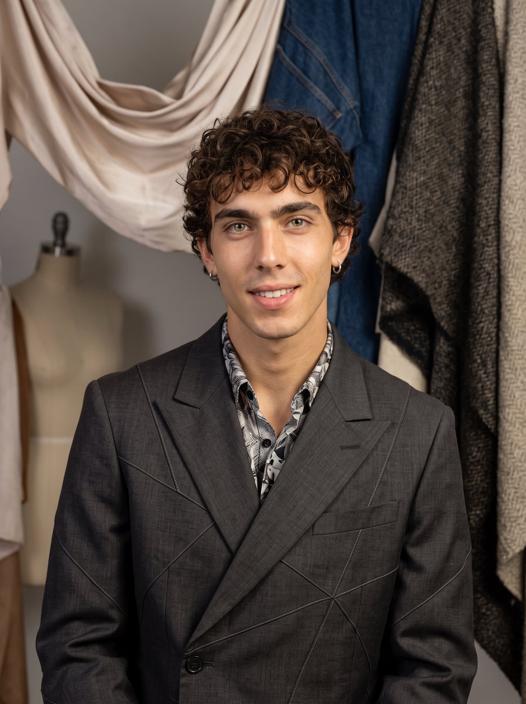 : Fashion designer headshot with a creative flair, capturing an man in trendy, avant-garde attire, against a fabric-rich background, exuding style and innovation for a Glassdoor profile.