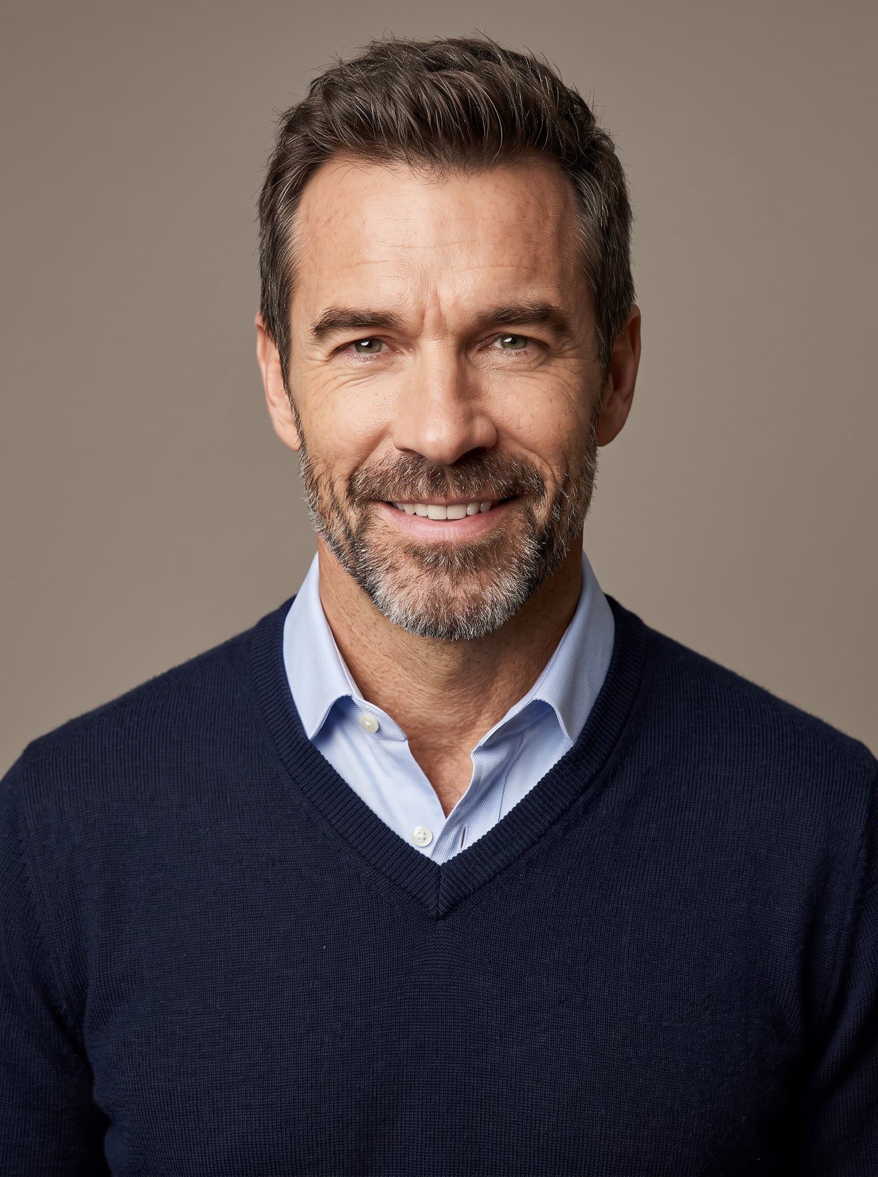 Produce a headshot of wearing a classic v-neck sweater with a collared shirt underneath, exuding professionalism and warmth, set against a neutral taupe background with soft, natural lighting.