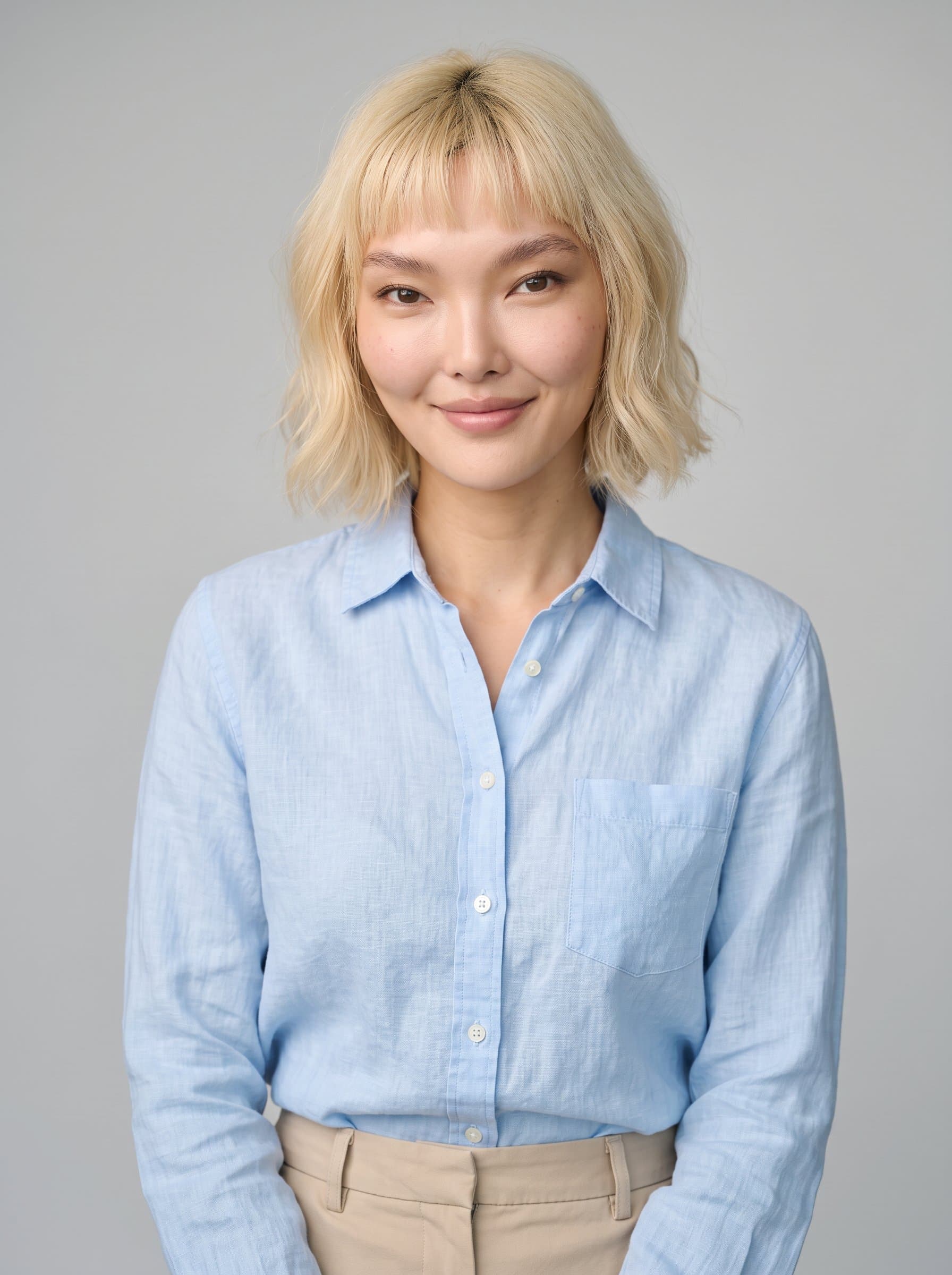 Create a photo of in a smart-casual ensemble, featuring a stylish button-down shirt, with a soft smile and engaging eyes, against a smooth, light gray background illuminated by soft ambient light.