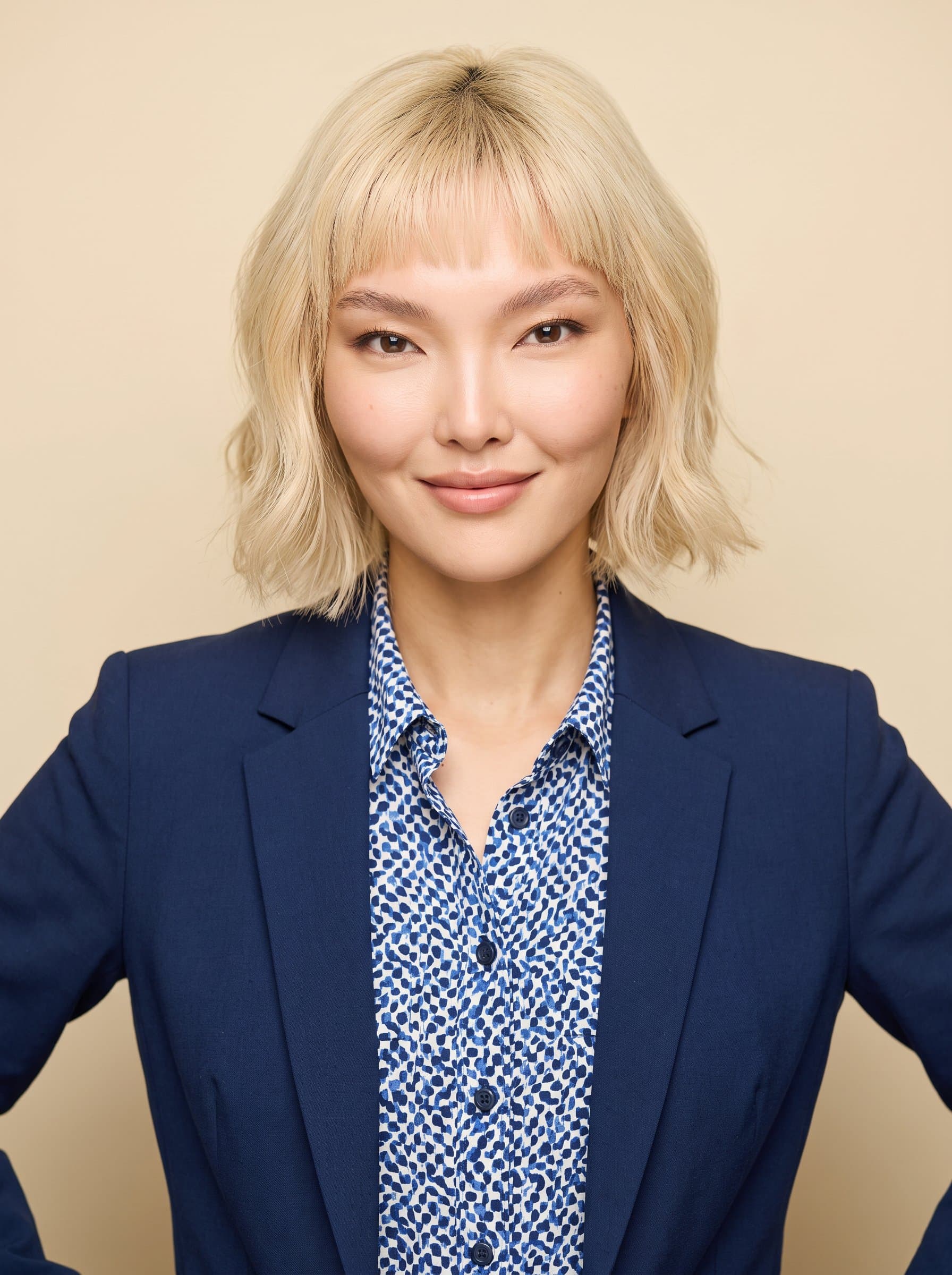 Design a headshot of with neatly styled hair and a confident stance, wearing a patterned shirt under a solid blazer, set against a cream-colored background with soft, even lighting.