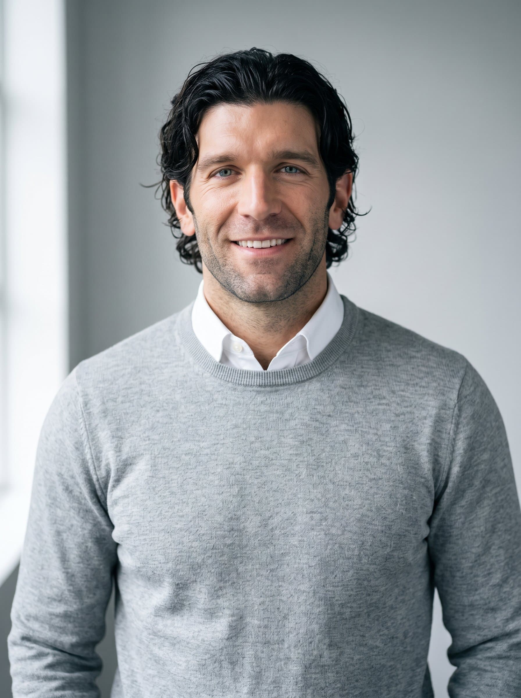 Design 's headshot, featuring them in a modern business-casual look with a light sweater over a shirt, set against a subtle, light gray backdrop, illuminated by soft, natural lighting.