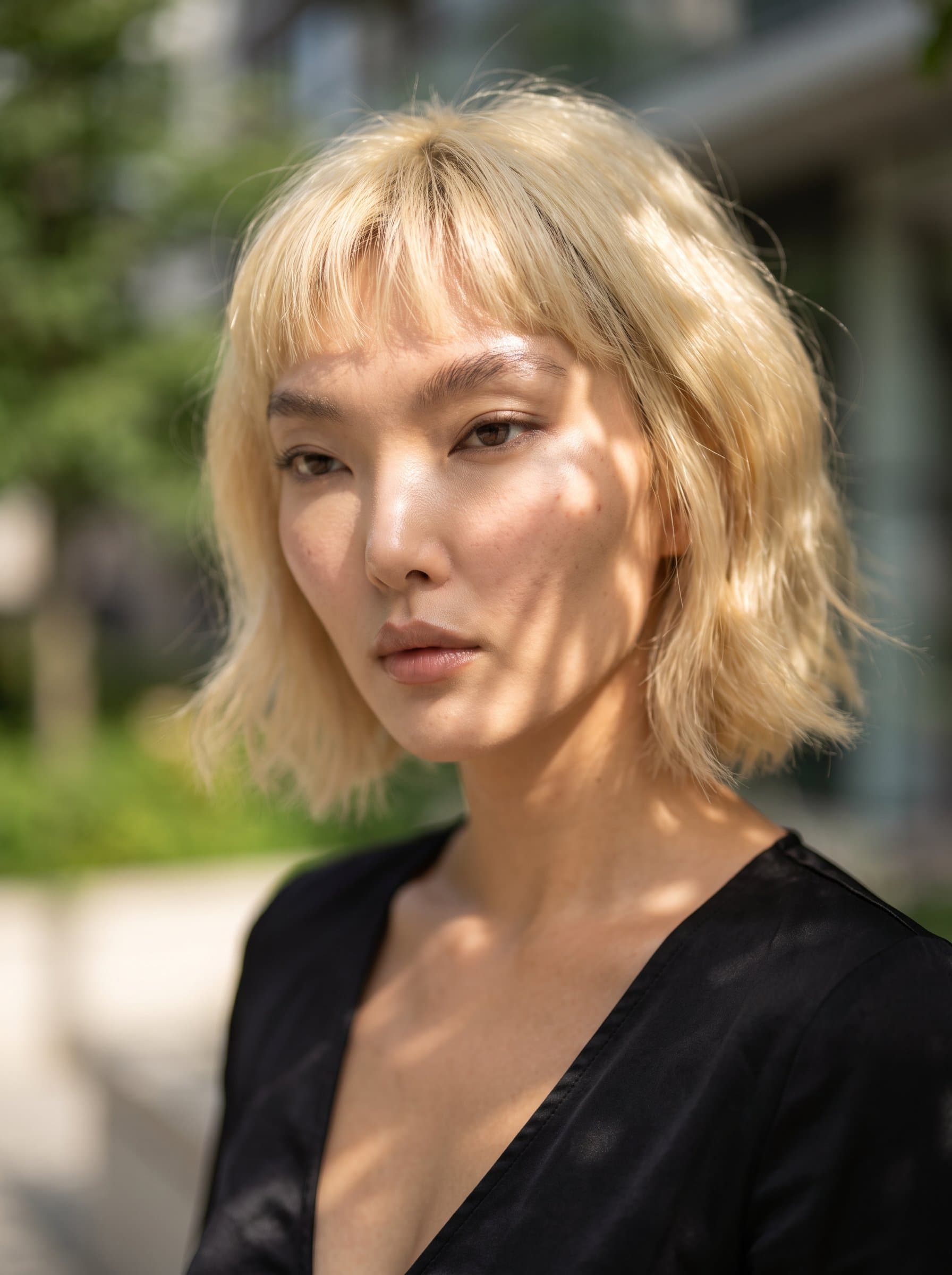 : Compose an artistic headshot featuring a thoughtful expression, with sunlight dappling the face. A seamless transition between the woman and a soft-focus background creates an ethereal, yet professional look.