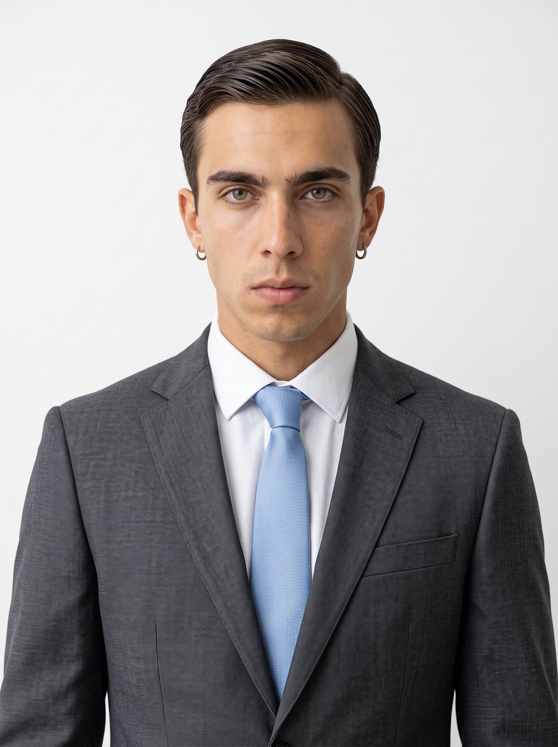 depicts a focused man with short, sleek hair and a neutral expression. Dressed in a charcoal suit and a light blue tie, they exude professionalism against a solid white background.
