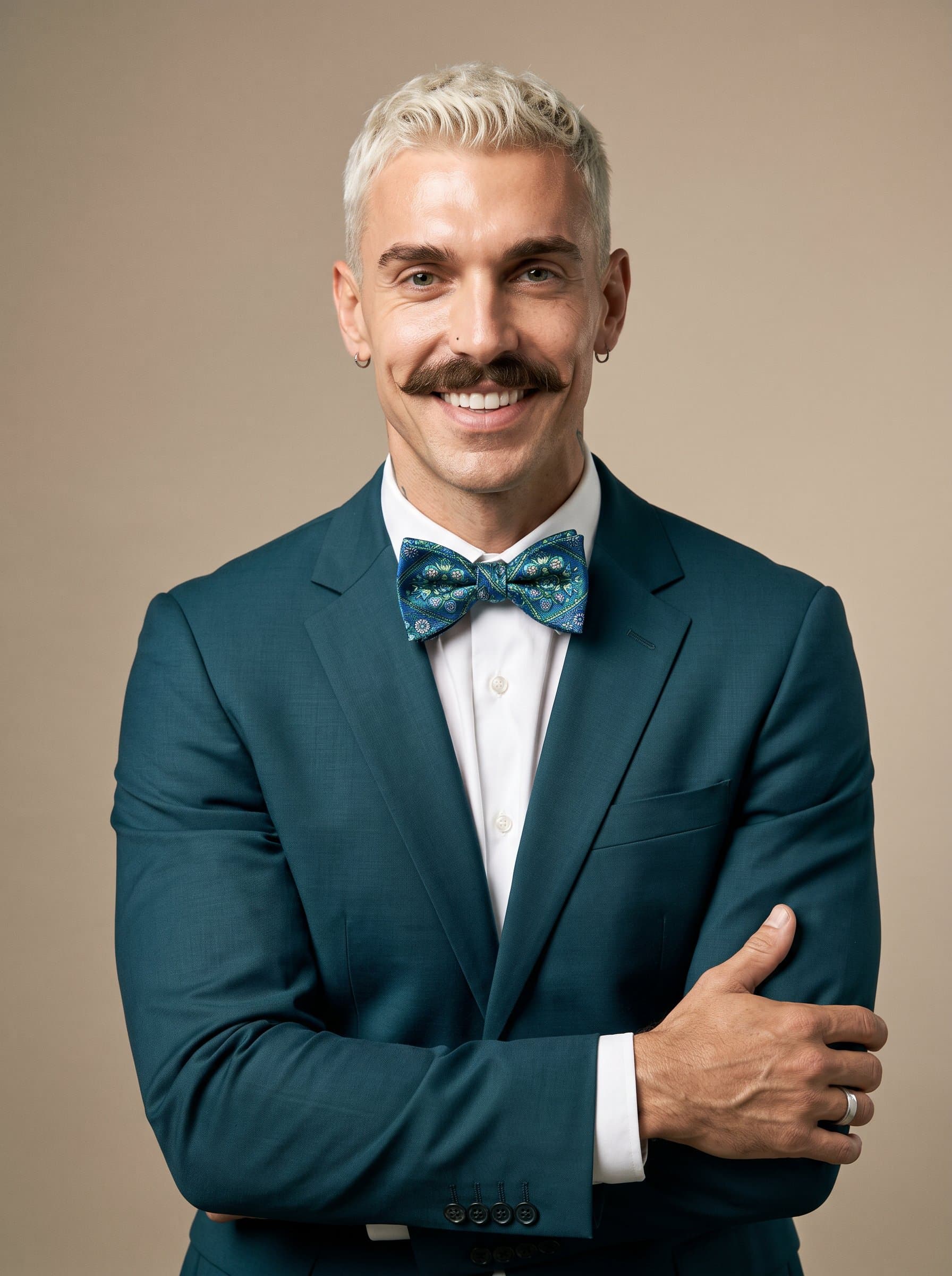 Presenting an man with a snappy bowtie and a dark teal suit, their smile emits charisma against the muted light brown background.