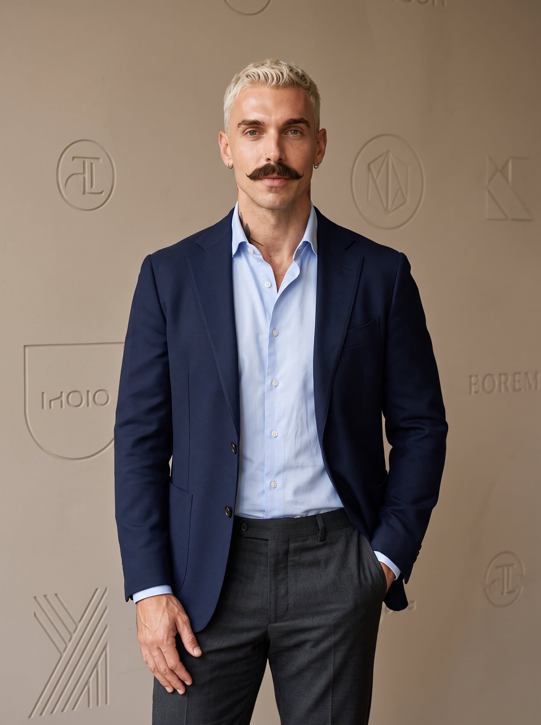 against a neutral-toned wall with subtle brand elements, showcasing a poised and professional demeanor. The expression is calm and assured, hinting at a collaborative leadership style.