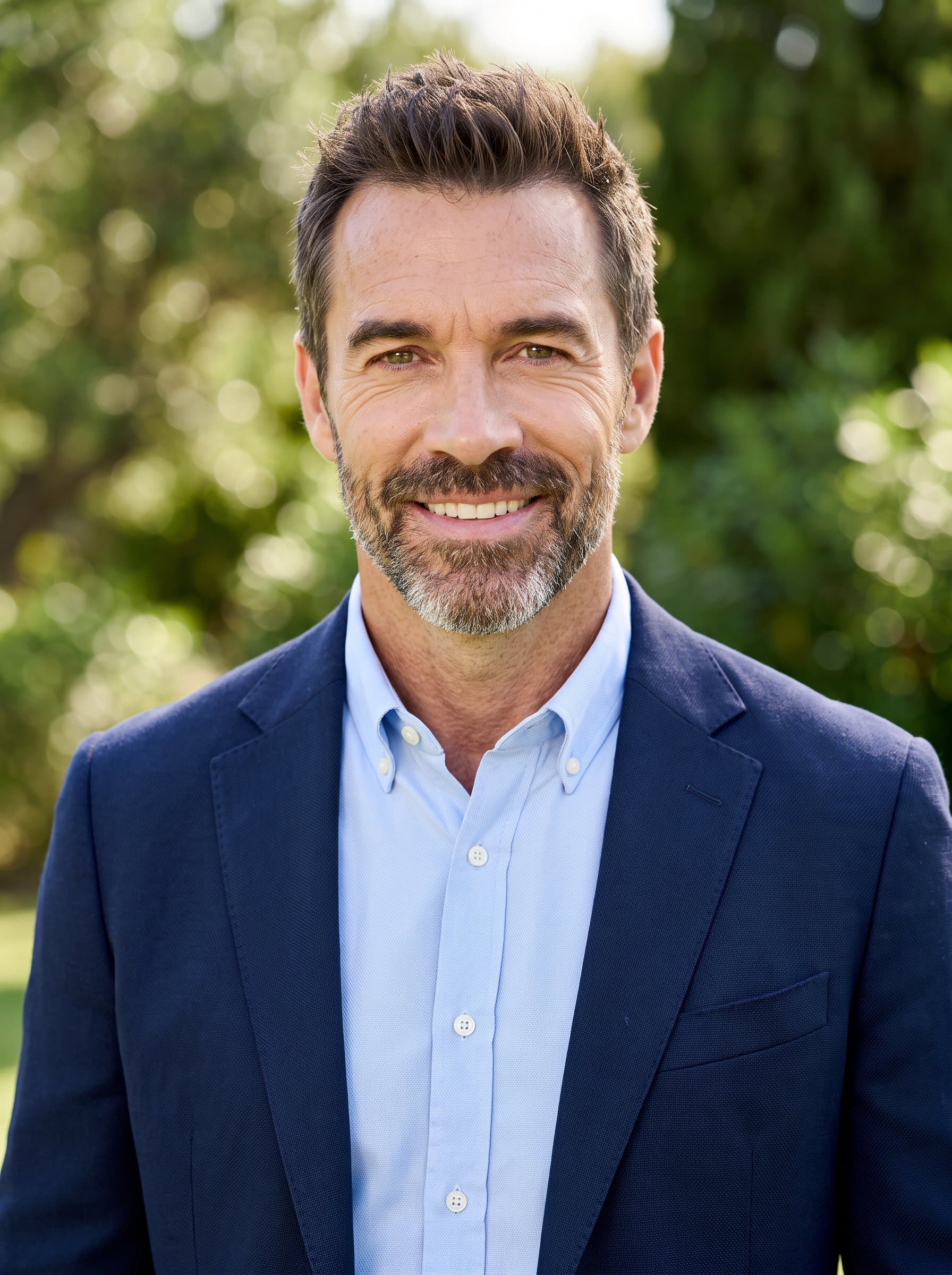 Against a soft-focus background of lush greenery, 's headshot showcases a natural, approachable feel. The attire is semi-formal, and the gentle outdoor lighting enhances the warmth in the face and smile.