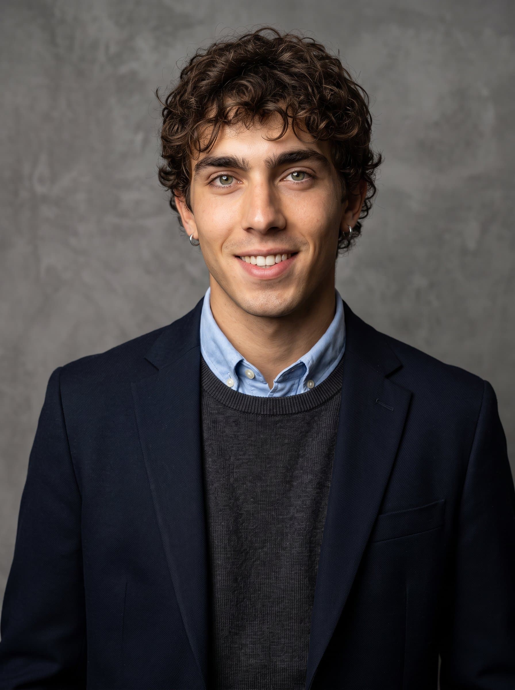 with a charming, confident smile, stands in front of a monochromatic feature wall. The smart-casual attire and excellent lighting create a professional, inviting headshot for any business setting.